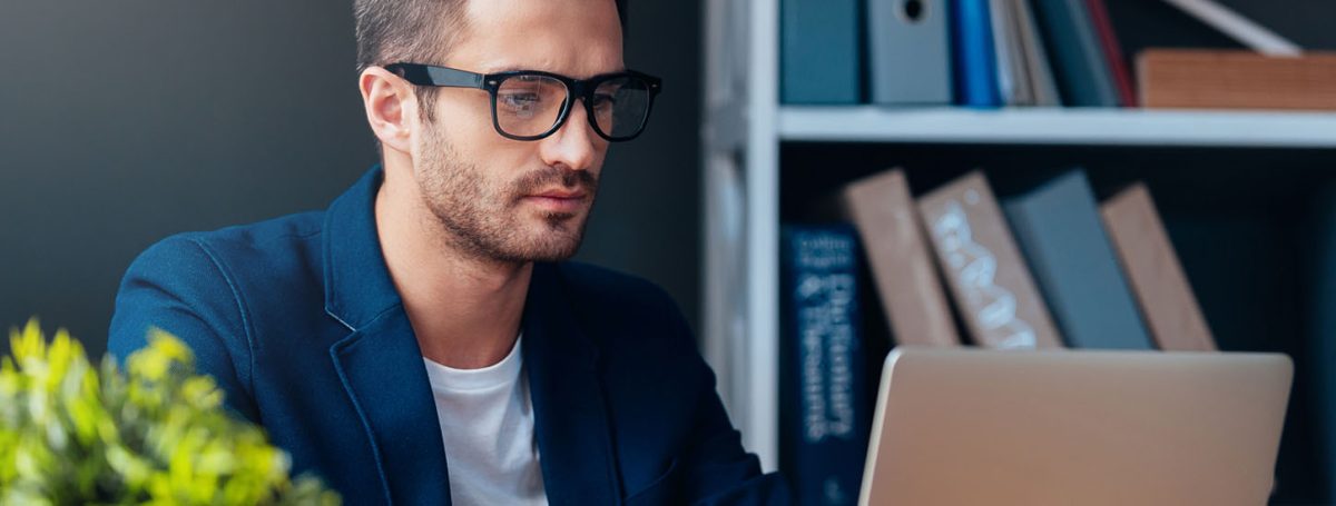 Businessman at work. Concentrated young man working on laptop while sitting at his working place in office