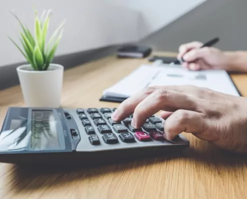 Businessman working on a graph document financial report and analysis calculation investment cost with calculator at office desk and other objects around\.